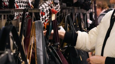 Parlak bir çanta dükkanından el çantası seçen kadın elleri yakından görülüyor..