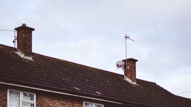 Çatıda bulutlu gökyüzünün altında antenler ve bacalar karamsar bir atmosfer yaratıyor.