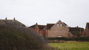 Yerleşim binaları ön planda yeşillik ve yukarıda bulutlu gökyüzü ile görülebilir.