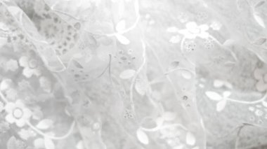 Çiçek desenleri ve parıltılı süslemeler içeren beyaz dantelli kumaş yakın plan.