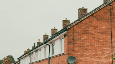 Yerleşim yerlerindeki tuğla binalarda bulutlu bir arkaplan karşısında bacalar var.