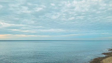 Huzurlu okyanus manzarası bulutlu bir gökyüzü ve su kenarında çakıllı bir plaj.