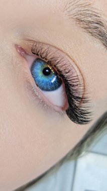 Kirpik uzantıları ve parlak mavi bir iris olan bir insan gözünün yakın görüntüsü