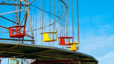 Açık mavi gökyüzüne karşı kırmızı ve sarı koltuklu boş renkli salıncak.