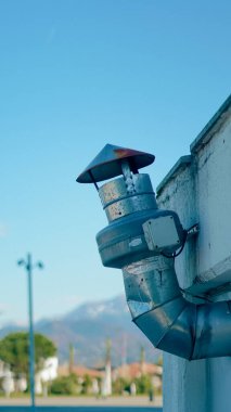 Duvara bağlı metal egzoz borusu, açık mavi gökyüzü ve arka planda dağlar.