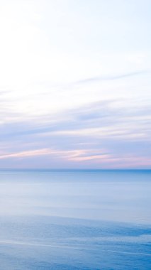 Huzurlu okyanus manzarası... Pastel bir gökyüzü ve şafak vakti pürüzsüz su yüzeyi.