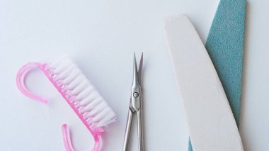 Beyaz bir yüzeyde gösterilen çivi bakım araçları makas, dosya ve temizlik fırçasını içerir