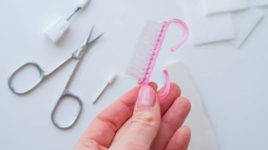 Beyaz bir yüzey üzerinde pembe kirpik fırçasıyla güzellik aletlerini tutan bir elin yakın çekimi