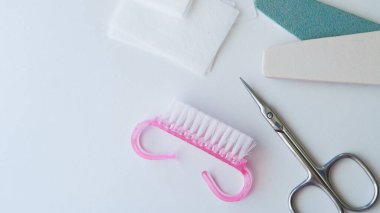 Beyaz bir yüzeye yerleştirilmiş pembe fırça, makas ve dosyalar gibi çivi bakım araçları