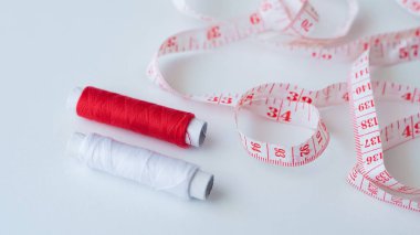Beyaz bir yüzey üzerinde ölçüm bandının yanında iki adet kırmızı ve beyaz dikiş ipi var.