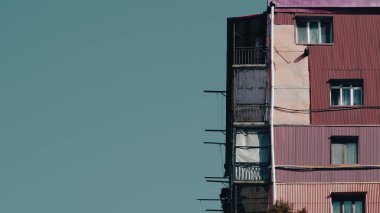 Açık mavi gökyüzüne karşı renkli ve balkonlu çok katlı bir apartman.