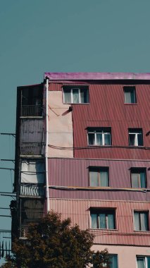 Açık gökyüzüne karşı çeşitli pencere stilleri ve balkonları olan çok renkli bir apartman.