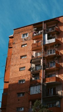 Açık mavi gökyüzüne karşı balkonları ve pencereleri olan çok katlı bir apartman.