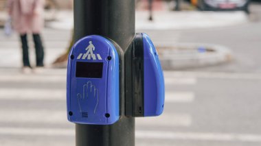 Şehir sokaklarında bir direğe bağlı mavi yaya geçidi sinyal düğmesi