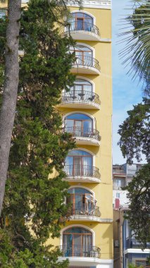Birden fazla balkonlu ve yemyeşil ağaçlarla çevrili şehir sarı binası.