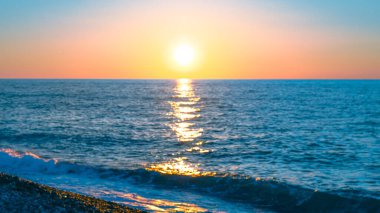 Canlı günbatımı, su yüzeyindeki yansımalarla okyanus dalgalarını aydınlatır.