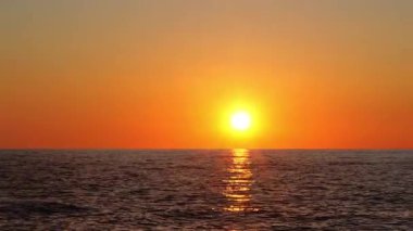 Canlı renklerle ve güneş ışığını yansıtan bulutlarla okyanusun üzerinde gün batımı manzarası