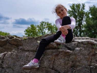 Küçük kız bir kayanın üzerinde tek başına oturuyor.