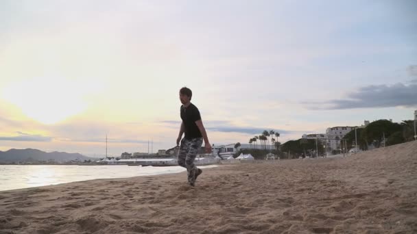 Ung man gör akrobatiska tricks på stranden. — Stockvideo