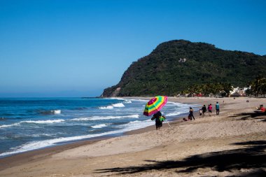 Lo de Marcos, Nayarit, Meksika - 23 Ocak 2021: Bir adam Meksika 'nın Riviera Nayarit sahilinde elinde gökkuşağı şemsiyesi ile kumlu sahilde yürüyor