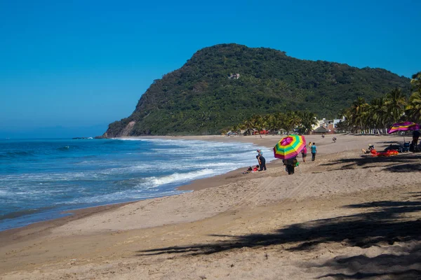 Lo de Marcos, Nayarit, Meksika - 23 Ocak 2021: Bir adam Meksika 'nın Riviera Nayarit sahilinde elinde gökkuşağı şemsiyesi ile kumlu sahilde yürüyor