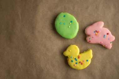 Kahverengi el işi kağıt yüzeyinde üç tane Paskalya temalı kurabiye. Tavşan, ördek, Paskalya yumurtası şekilleri bahar renklerinde pembe, sarı ve yeşil.