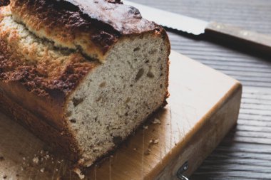 Arka planda bir bıçakla kesme tahtasının üzerinde taze pişmiş muz ekmeği..