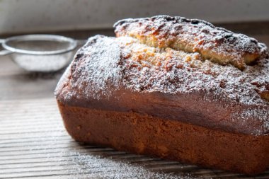 Tahta bir tezgahın üzerinde duran toz şekerle tozlanmış taze bir somun muzlu cevizli ekmek.