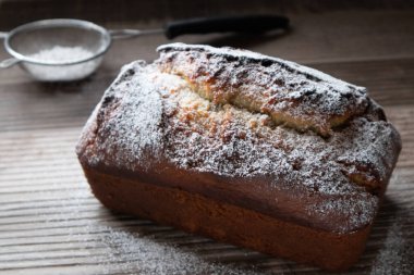 Tahta bir tezgahın üzerinde duran toz şekerle tozlanmış taze bir somun muzlu cevizli ekmek.