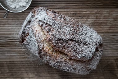Tahta bir tezgahın üzerinde duran toz şekerle tozlanmış taze bir somun muzlu cevizli ekmek.