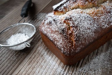 Tahta bir tezgahın üzerinde duran toz şekerle tozlanmış taze bir somun muzlu cevizli ekmek.