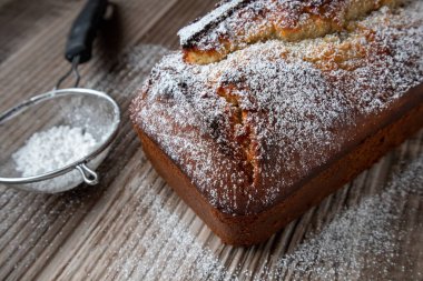 Tahta bir tezgahın üzerinde duran toz şekerle tozlanmış taze bir somun muzlu cevizli ekmek.