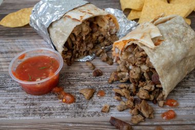 Carne asada bifteği burrito ikiye bölünür ve patates kızartması ve salsa sosuyla ahşap bir masada oturur..
