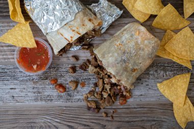 Carne asada bifteğinin tepesinden et dökülerek ikiye bölünmüş. Patates kızartması ve salsa sosuyla ahşap bir masada..