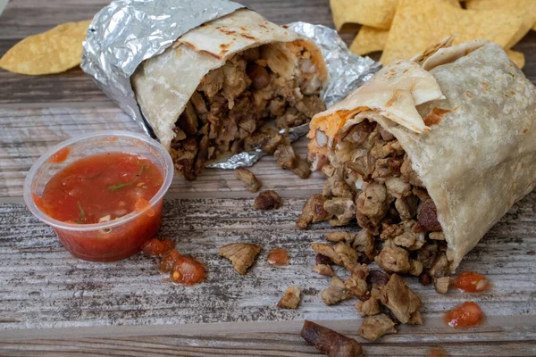 Carne asada bifteği burrito ikiye bölünür ve patates kızartması ve salsa sosuyla ahşap bir masada oturur..
