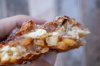 Elmalı börek tutan bir el, içinde elma ve tarçın parçalarını ahşap bir arka planın önünde gösteriyor.