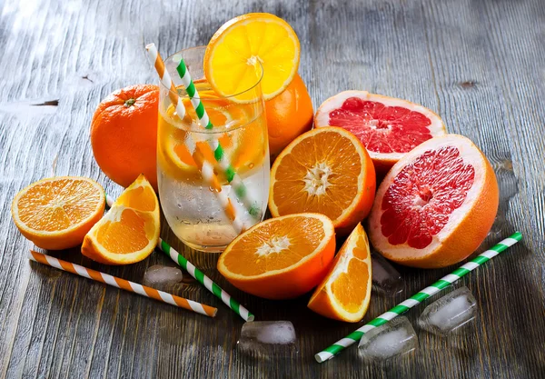 Naranja fresca y pomelos con vaso de agua y pajitas — Foto de Stock