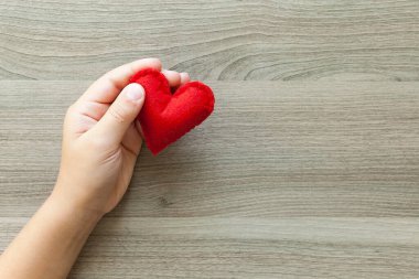 Keçeden kırmızı bir kalp tutan eller.