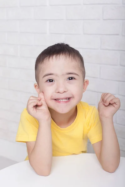 Rapaz bonito com síndrome de Down em óculos sentado, sorrindo para a câmera e jogando — Fotografia de Stock