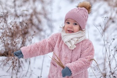 A little girl in a pink fur coat is having fun, playing outside, surrounded by snow. Winter time, the concept of healthy children's activity