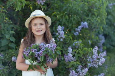 Leylak bahçesinde hasır şapkalı güzel bir kız. Baharda leylak çiçekli bir kız. Bahçıvanlık.