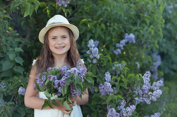Leylak bahçesinde hasır şapkalı güzel bir kız. Baharda leylak çiçekli bir kız. Bahçıvanlık.