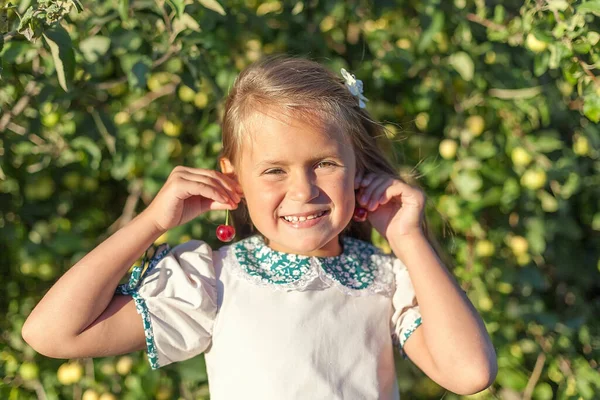 リンゴ園の子供の肖像画 ピンクのシャツとデニムのスカートを着た女の子は リンゴの木の枝を背景に 耳のような彼女の手にリンゴを持っています 子供の世話をする幸せな子供 — ストック写真