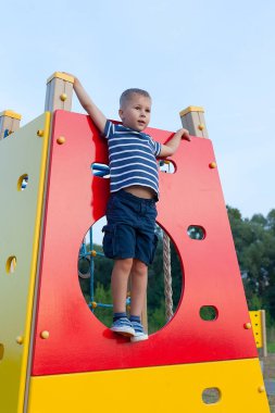Küçük beyaz çocuk oyun parkında egzersiz yapmak için maymun barına asılmış..