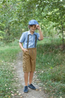 Yaz parkında palmiye ağaçlarıyla poz veren genç bir çocuk. Sevimli, gözlüklü, gülümseyen, 13 yaşında, kameraya bakan genç bir çocuk. Çocuğun açık hava portresi..