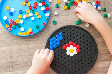 Çocukların elleri renkli mozaiklerin detaylarını masanın üzerindeki çiçek çizimine koyuyor. Hapisteki çocuğun boş vakitleri. Tablo oyunu.