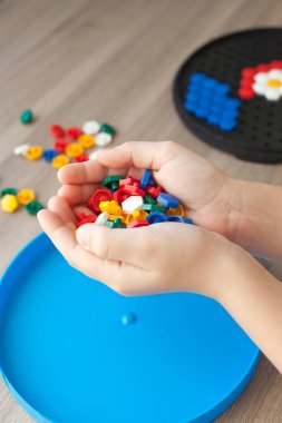 Çocukların elleri renkli mozaiklerin detaylarını masanın üzerindeki çiçek çizimine koyuyor. Hapisteki çocuğun boş vakitleri. Tablo oyunu.