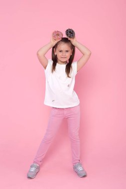 Heyecanlı sarışın kız, elinde iki donutla şeker kalorisi ve sağlıksız beslenme bağımlılığıyla oynayarak gözlerinin içine bakıyor.