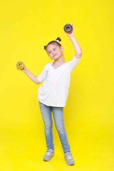 Retrato de uma menina alegre com uma bandana engraçada se divertindo em direção à câmera com donuts coloridos isolados em um fundo rosa. Expressão de emoções positivas verdadeiras de uma criança bonita — Fotografia de Stock