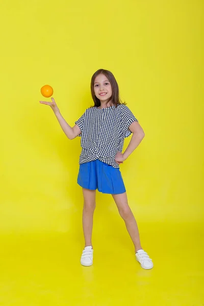 Primer plano retrato del estudio de la niña sonriendo sosteniendo mitades de naranjas en sus ojos. Azul aislado. Foto vertical —  Fotos de Stock